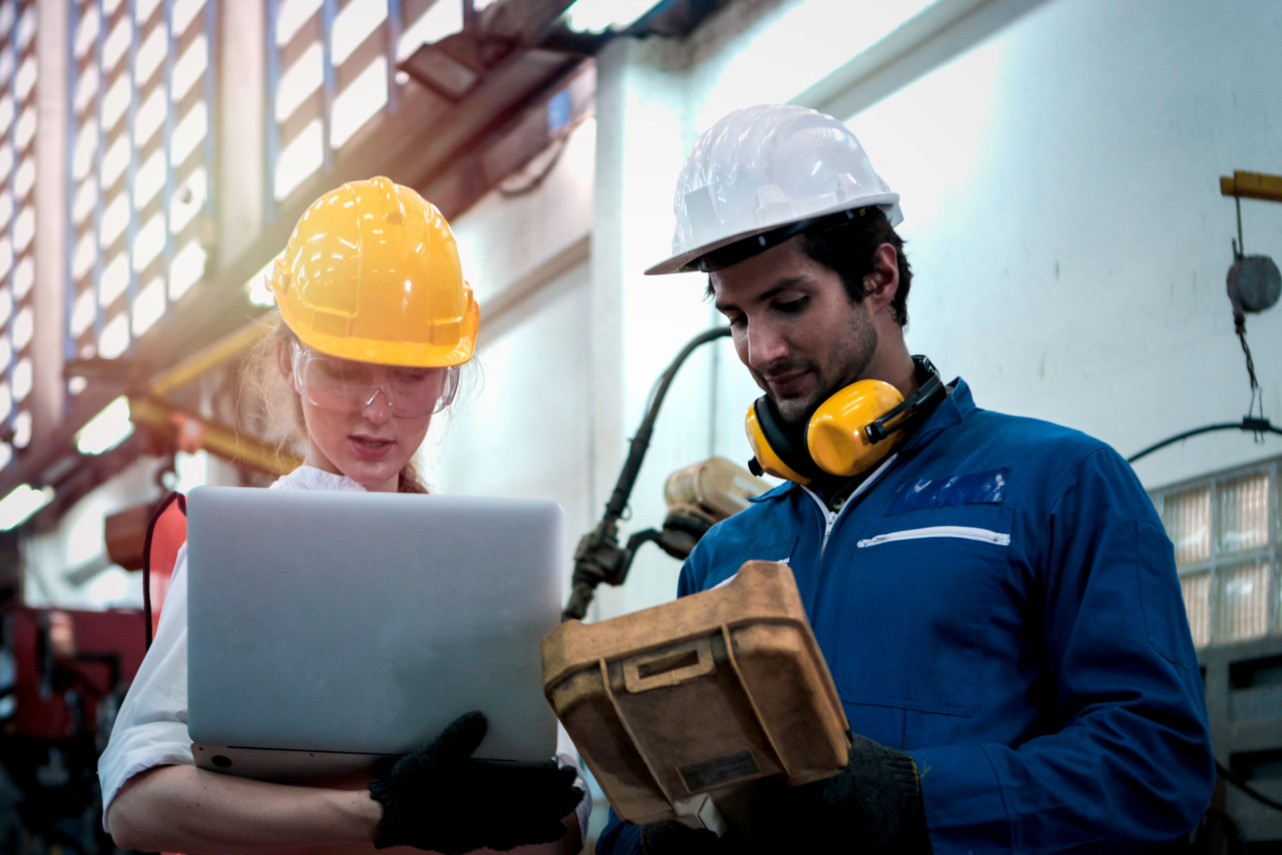 Woman and man wearing hard hats are discussing work at a manufacturing facility